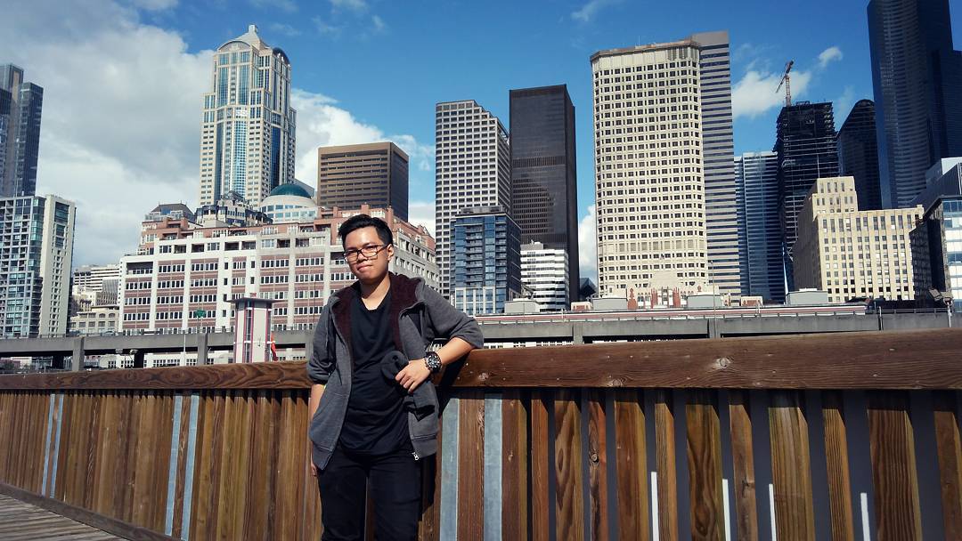 Landscape photo of a person on a pier with waterfront skyscrapers in the background.